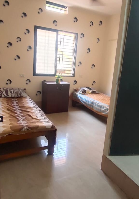Clean and brightly lit twin-sharing Boys PG room in Hubli, showing two wooden beds, a central storage unit, and a large window for ample natural light.